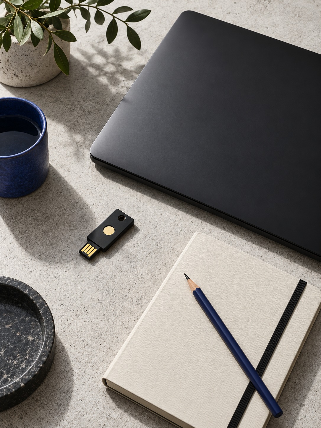 Closed laptop with a hardware security key and notebook on concrete