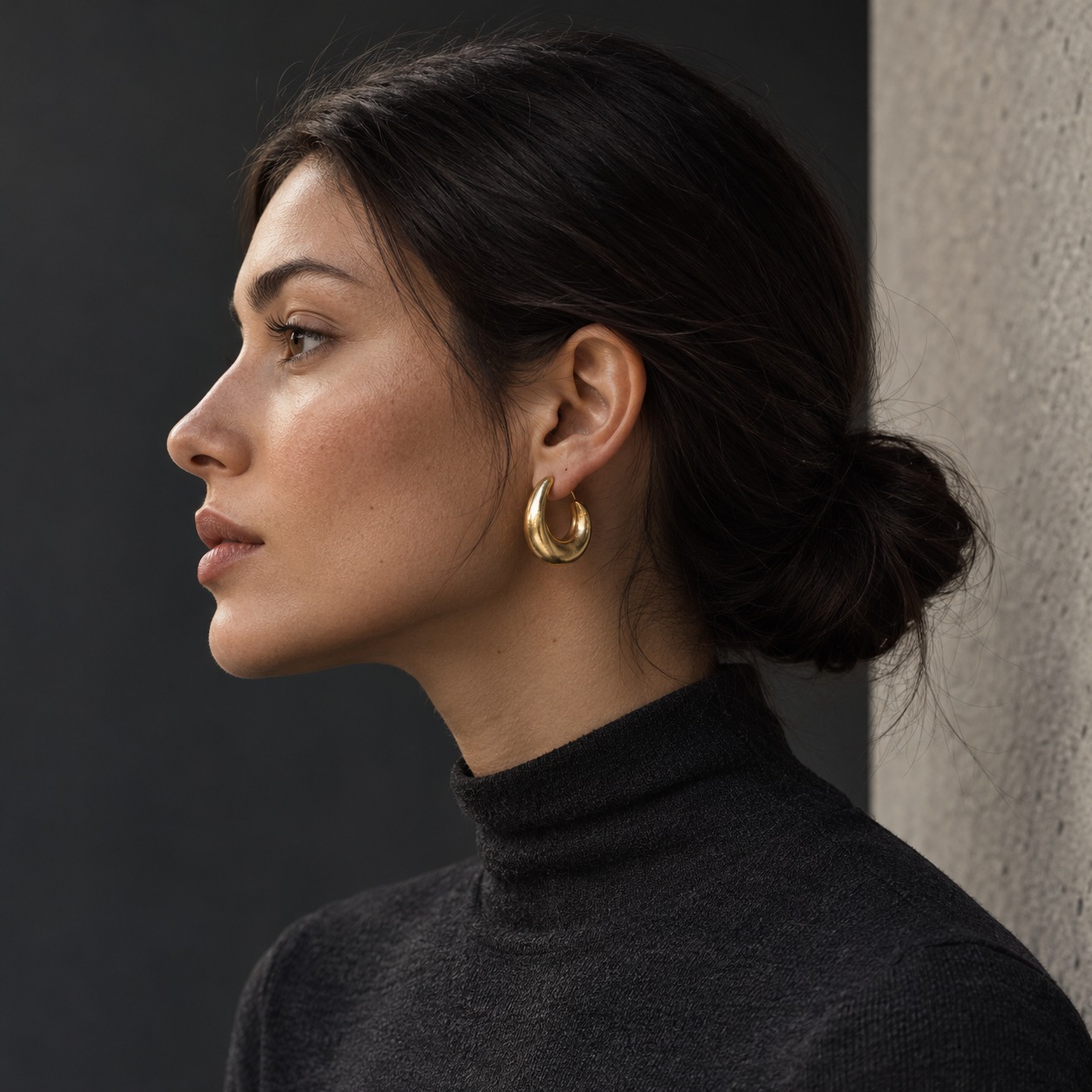 Sculptural gold-plated hoop earrings Side-profile portrait with tied-back hair and medium sculptural gold-plated hoop earrings against a graphite studio backdrop. | Sky Rye Design Side-profile portrait with tied-back hair and medium sculptural gold-plated hoop earrings against a graphite studio backdrop.